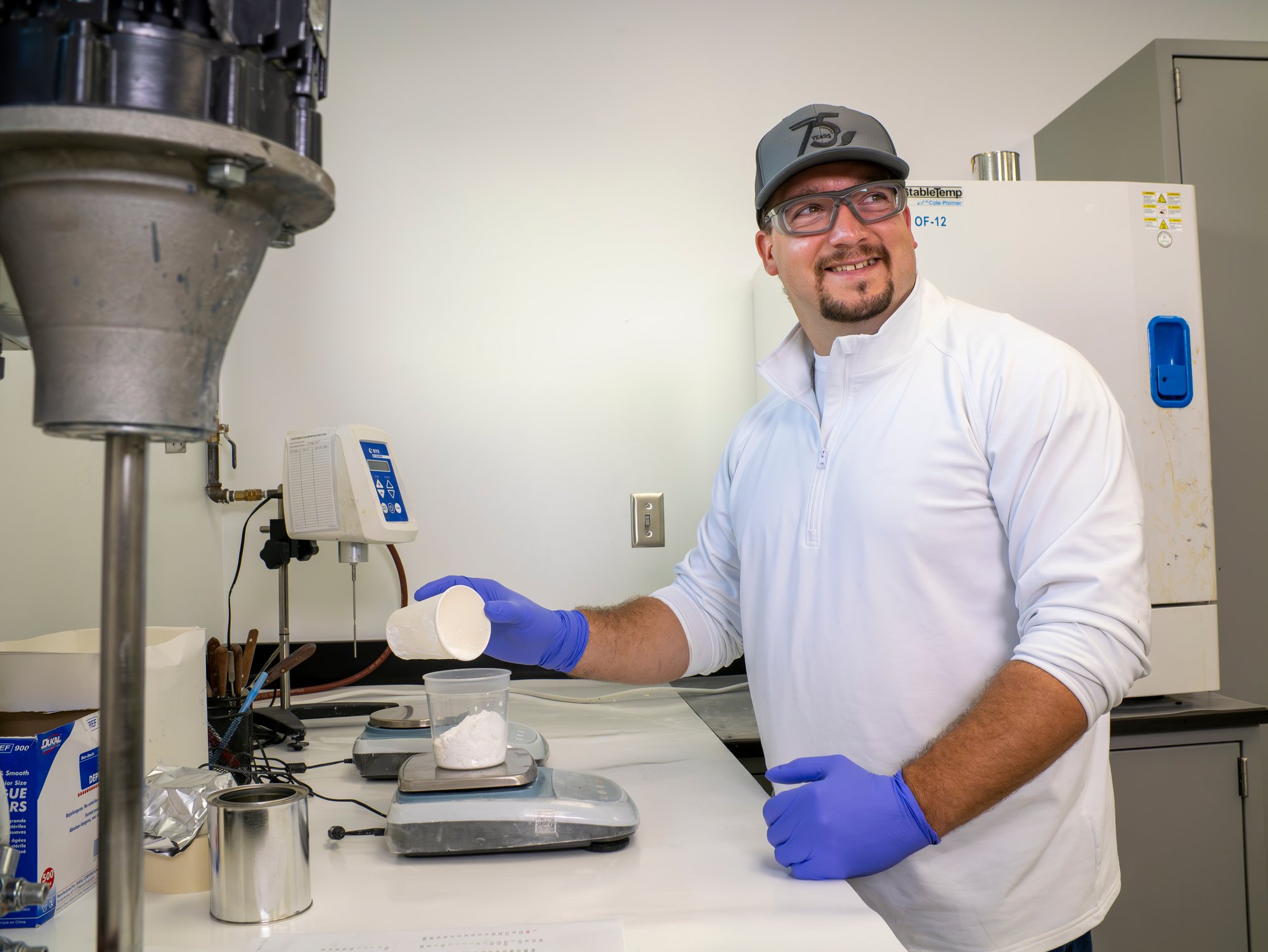 A man in a laboratory wearing gloves and weighing a powder